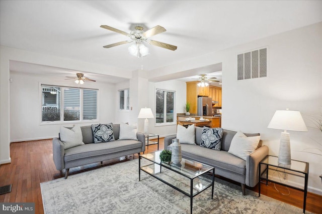 living room featuring visible vents, baseboards, a ceiling fan, and wood-type flooring