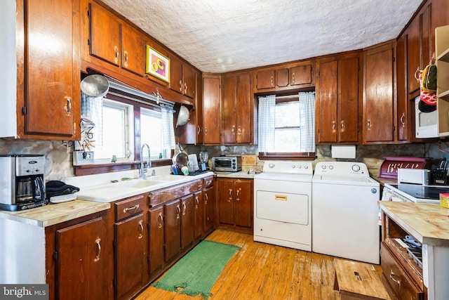 kitchen with light wood-type flooring, a sink, a textured ceiling, washing machine and dryer, and light countertops