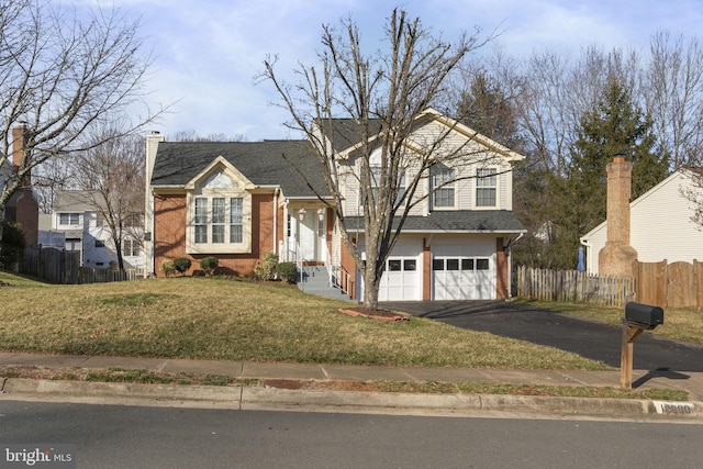 tri-level home with a shingled roof, a front lawn, fence, aphalt driveway, and an attached garage