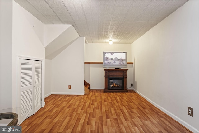 unfurnished living room featuring a glass covered fireplace, wood finished floors, and baseboards