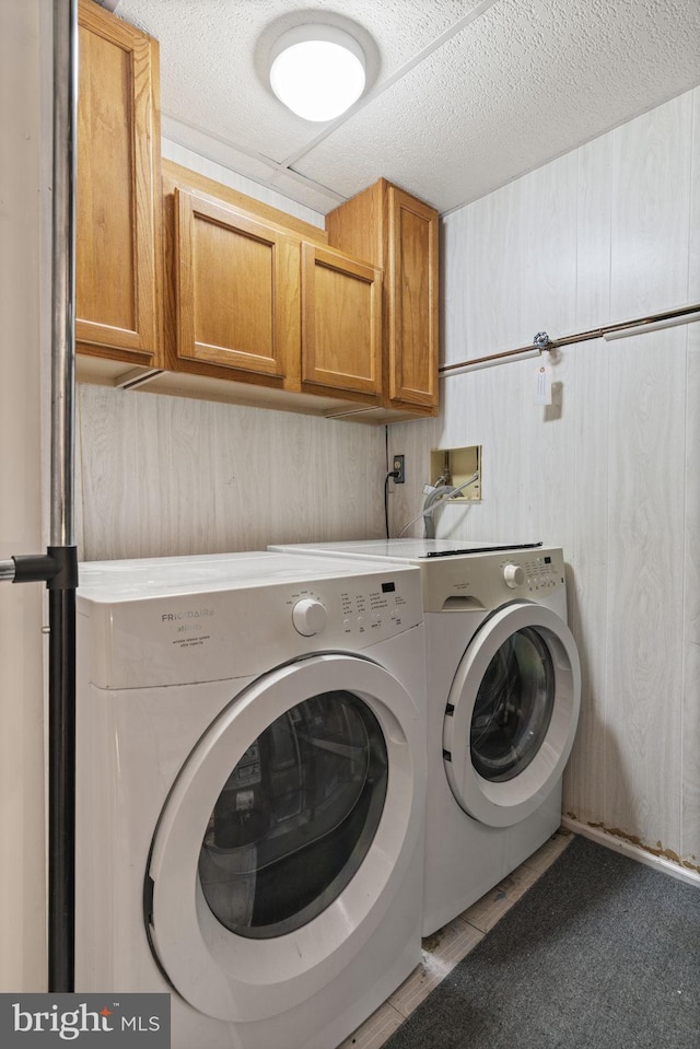 clothes washing area featuring a textured ceiling, cabinet space, and washing machine and clothes dryer