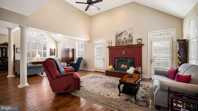 living room featuring a ceiling fan, wood finished floors, ornate columns, high vaulted ceiling, and a fireplace