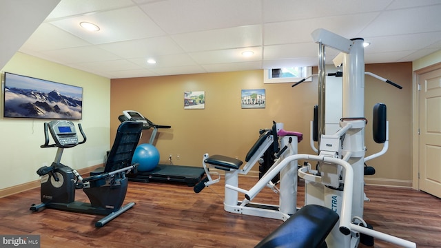 exercise room featuring a drop ceiling, recessed lighting, baseboards, and wood finished floors