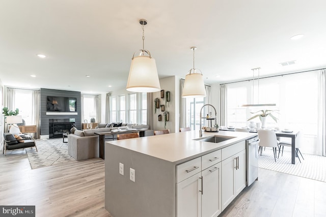 kitchen featuring an island with sink, a sink, light wood finished floors, dishwasher, and hanging light fixtures