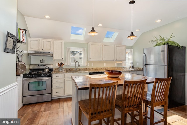 kitchen with under cabinet range hood, vaulted ceiling with skylight, light wood-style floors, stainless steel appliances, and a sink