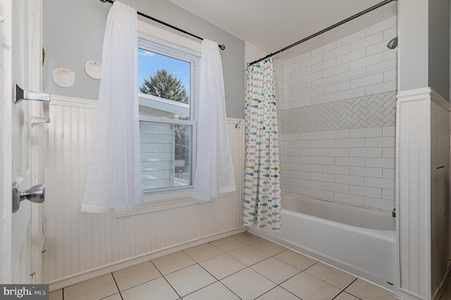 full bath with tile patterned flooring, shower / bathtub combination with curtain, and a wainscoted wall