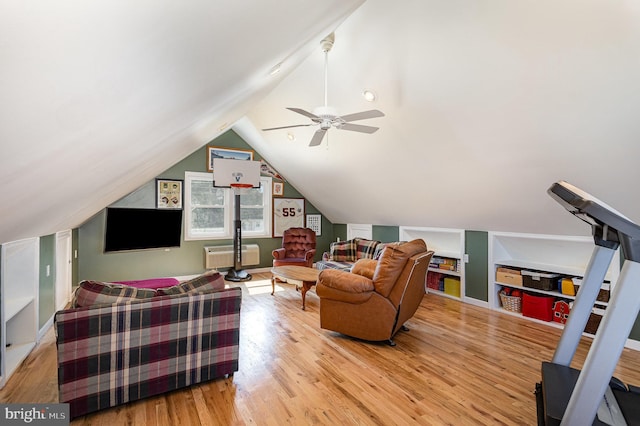 living room featuring a ceiling fan, light wood-type flooring, a wall unit AC, and vaulted ceiling