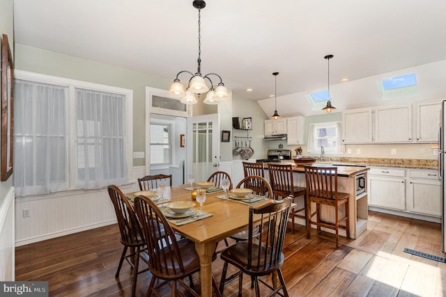 dining area with lofted ceiling, a notable chandelier, light wood-style flooring, and wainscoting