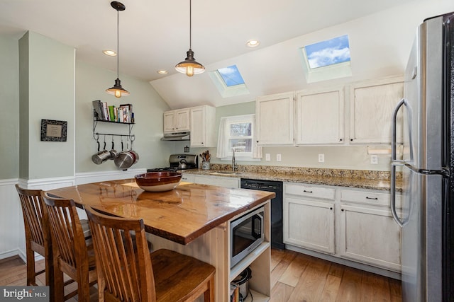 kitchen featuring under cabinet range hood, a sink, vaulted ceiling with skylight, appliances with stainless steel finishes, and light wood finished floors