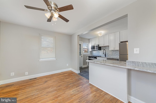 kitchen featuring backsplash, baseboards, light wood-style flooring, white cabinets, and stainless steel appliances