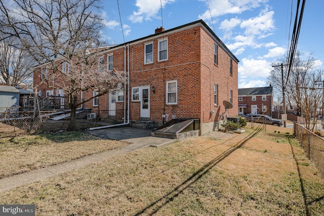 rear view of house featuring a lawn, fence, brick siding, central AC unit, and a chimney