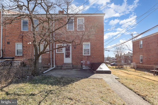 rear view of house featuring fence, a yard, a chimney, entry steps, and brick siding