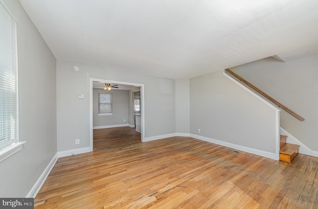 unfurnished living room with light wood-style flooring, a ceiling fan, stairs, and baseboards