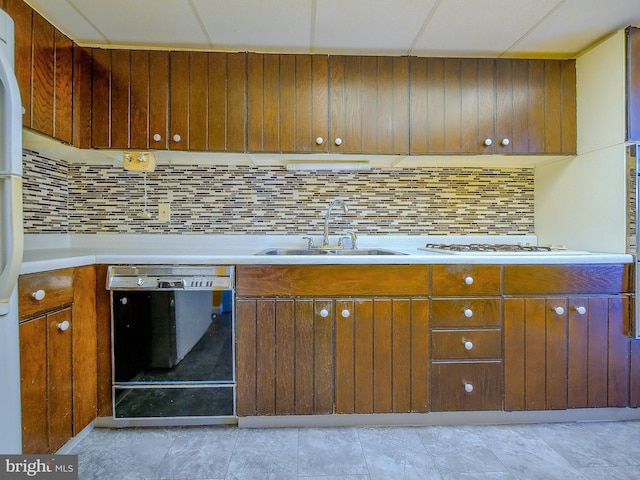 kitchen featuring backsplash, light countertops, brown cabinetry, white appliances, and a sink