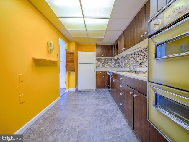 kitchen featuring tasteful backsplash, double oven, light countertops, freestanding refrigerator, and a paneled ceiling