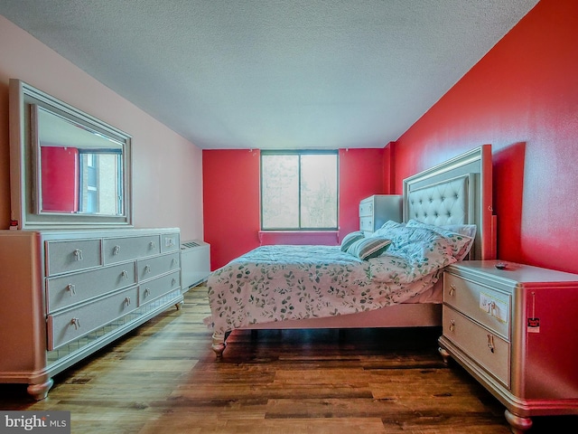 bedroom with multiple windows, a textured ceiling, wood finished floors, and radiator heating unit