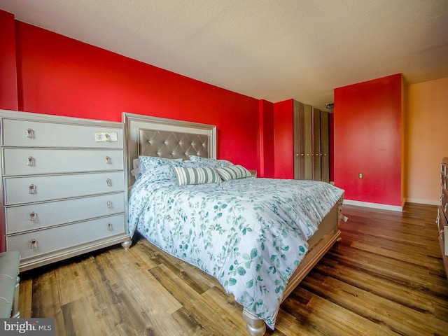 bedroom with wood finished floors, baseboards, and a textured ceiling