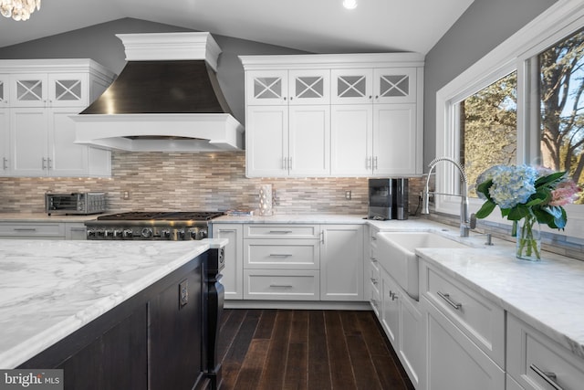 kitchen featuring premium range hood, dark wood-type flooring, a sink, white cabinetry, and vaulted ceiling