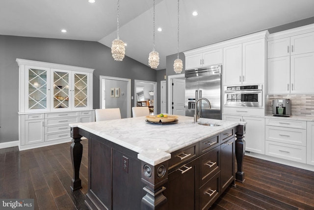 kitchen with dark wood finished floors, appliances with stainless steel finishes, a kitchen breakfast bar, white cabinets, and a sink