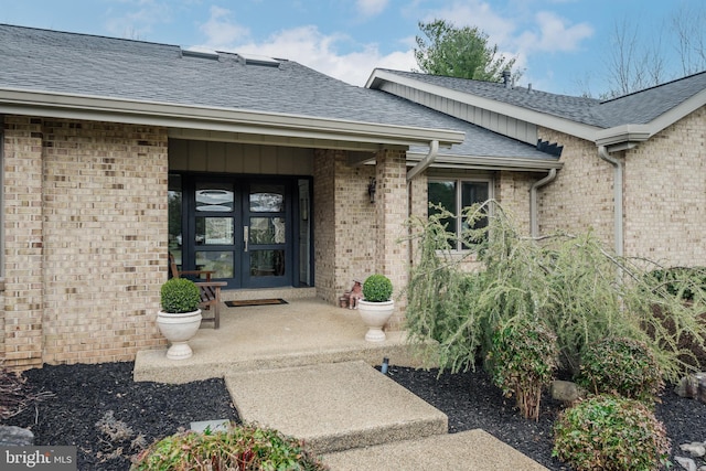 view of exterior entry featuring french doors, brick siding, and a shingled roof