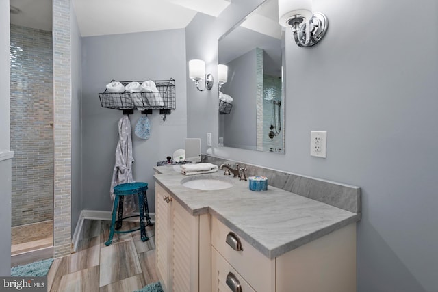 bathroom featuring wood finish floors, tiled shower, vanity, and baseboards