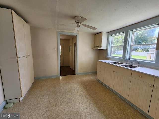 kitchen featuring baseboards, light floors, light countertops, a textured ceiling, and a sink