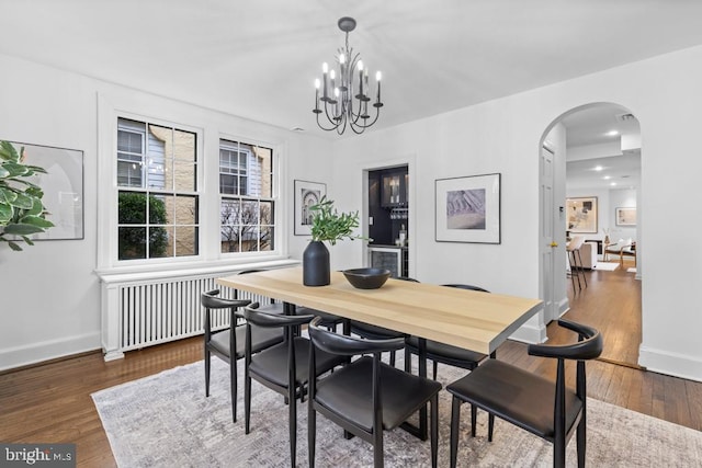 dining space with hardwood / wood-style floors, radiator, baseboards, and arched walkways