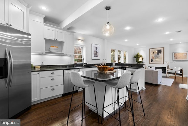 kitchen with a peninsula, dark wood-type flooring, appliances with stainless steel finishes, dark countertops, and a kitchen breakfast bar