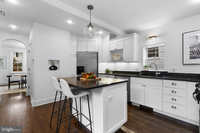 kitchen with a sink, stainless steel appliances, dark wood-type flooring, white cabinets, and dark countertops