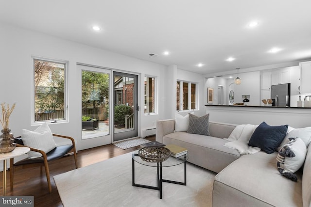 living room featuring recessed lighting, light wood-type flooring, baseboard heating, and visible vents