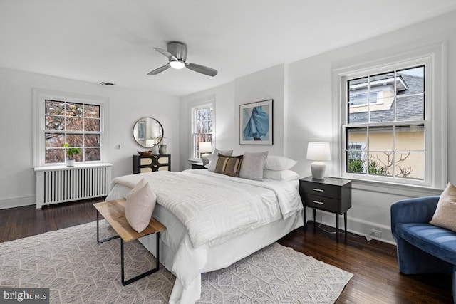 bedroom featuring baseboards, multiple windows, radiator, and wood finished floors