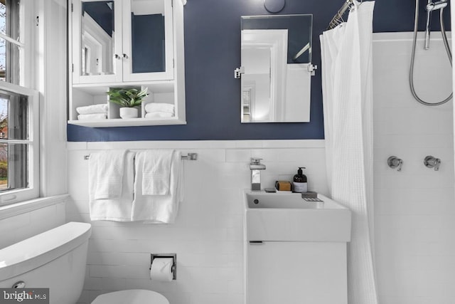 full bathroom featuring tile walls, a wainscoted wall, toilet, tiled shower, and vanity