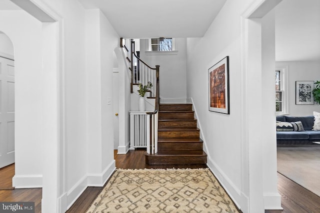 stairway featuring baseboards, arched walkways, wood finished floors, and radiator heating unit