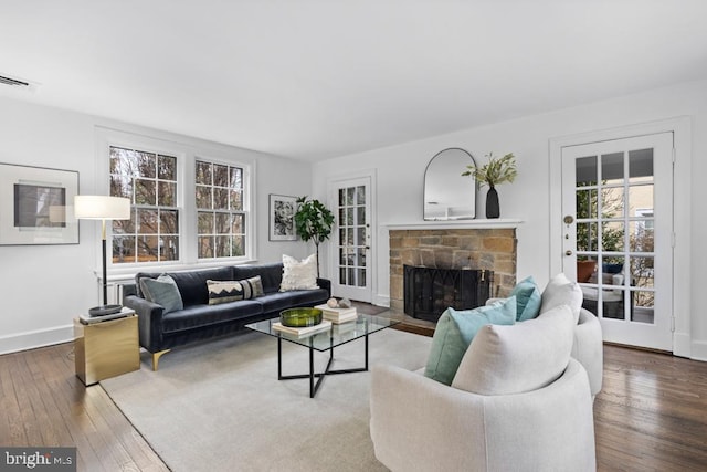 living area with a stone fireplace, baseboards, visible vents, and wood-type flooring