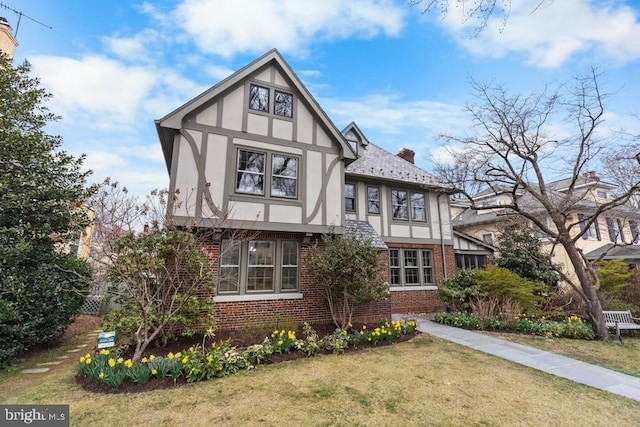 tudor house featuring brick siding, stucco siding, a chimney, and a front yard