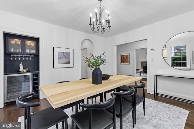 dining space featuring dark wood-type flooring, wine cooler, arched walkways, a bar, and a chandelier