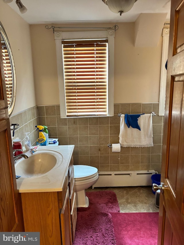 half bathroom with a baseboard heating unit, tile walls, vanity, and tile patterned flooring