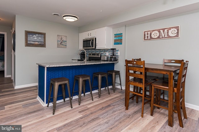 kitchen with light wood finished floors, a peninsula, stainless steel appliances, white cabinets, and tasteful backsplash