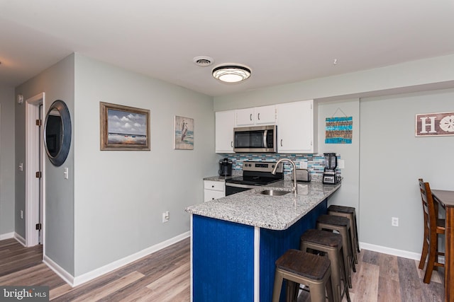 kitchen featuring a kitchen bar, a sink, white cabinetry, stainless steel appliances, and a peninsula