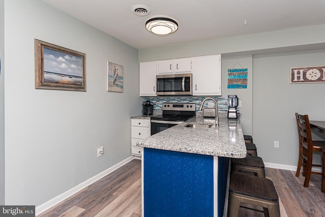 kitchen featuring visible vents, a breakfast bar, appliances with stainless steel finishes, white cabinets, and a sink