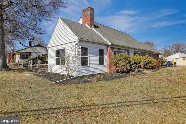 view of side of home with brick siding, a shingled roof, fence, a lawn, and a chimney