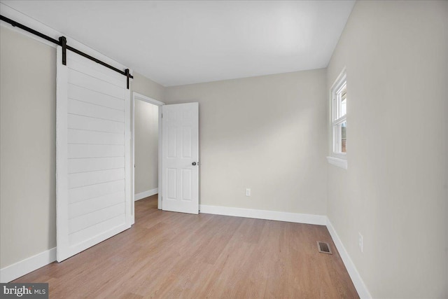 unfurnished bedroom with a barn door, wood finished floors, visible vents, and baseboards