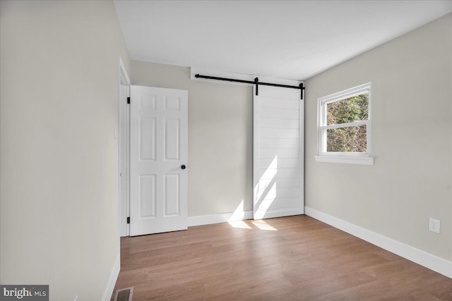 unfurnished bedroom featuring visible vents, a barn door, baseboards, and wood finished floors