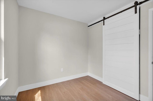 spare room with baseboards, a barn door, and wood finished floors