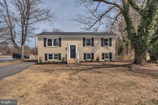 split foyer home with brick siding, driveway, and a front yard