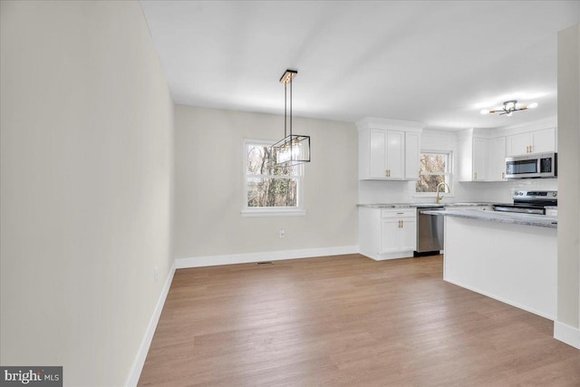 kitchen with light wood finished floors, white cabinets, appliances with stainless steel finishes, and baseboards