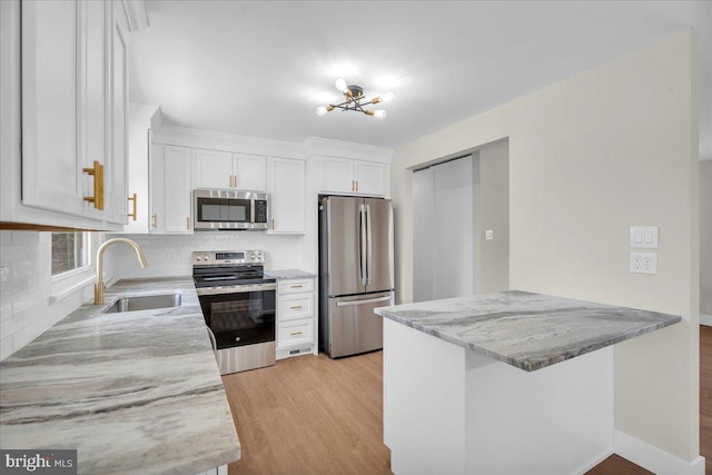 kitchen with light stone countertops, light wood-style flooring, a sink, appliances with stainless steel finishes, and white cabinetry