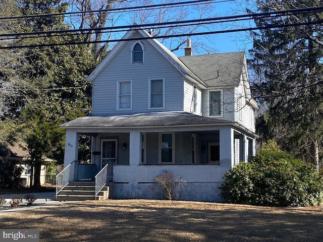 country-style home with roof with shingles, covered porch, and a chimney