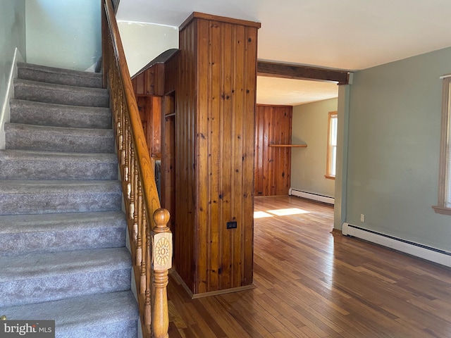 staircase with a baseboard heating unit, wooden walls, and wood-type flooring