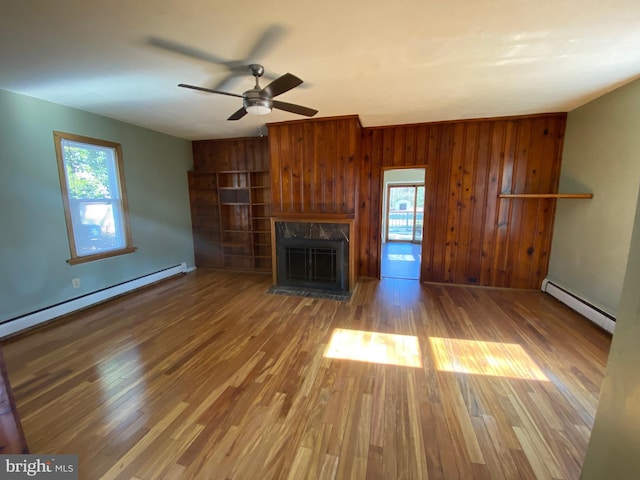 unfurnished living room with a wealth of natural light, baseboard heating, wood finished floors, and a fireplace